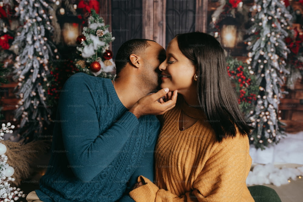 a man and woman kissing in front of a christmas tree