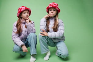 two young girls sitting on the ground wearing hats