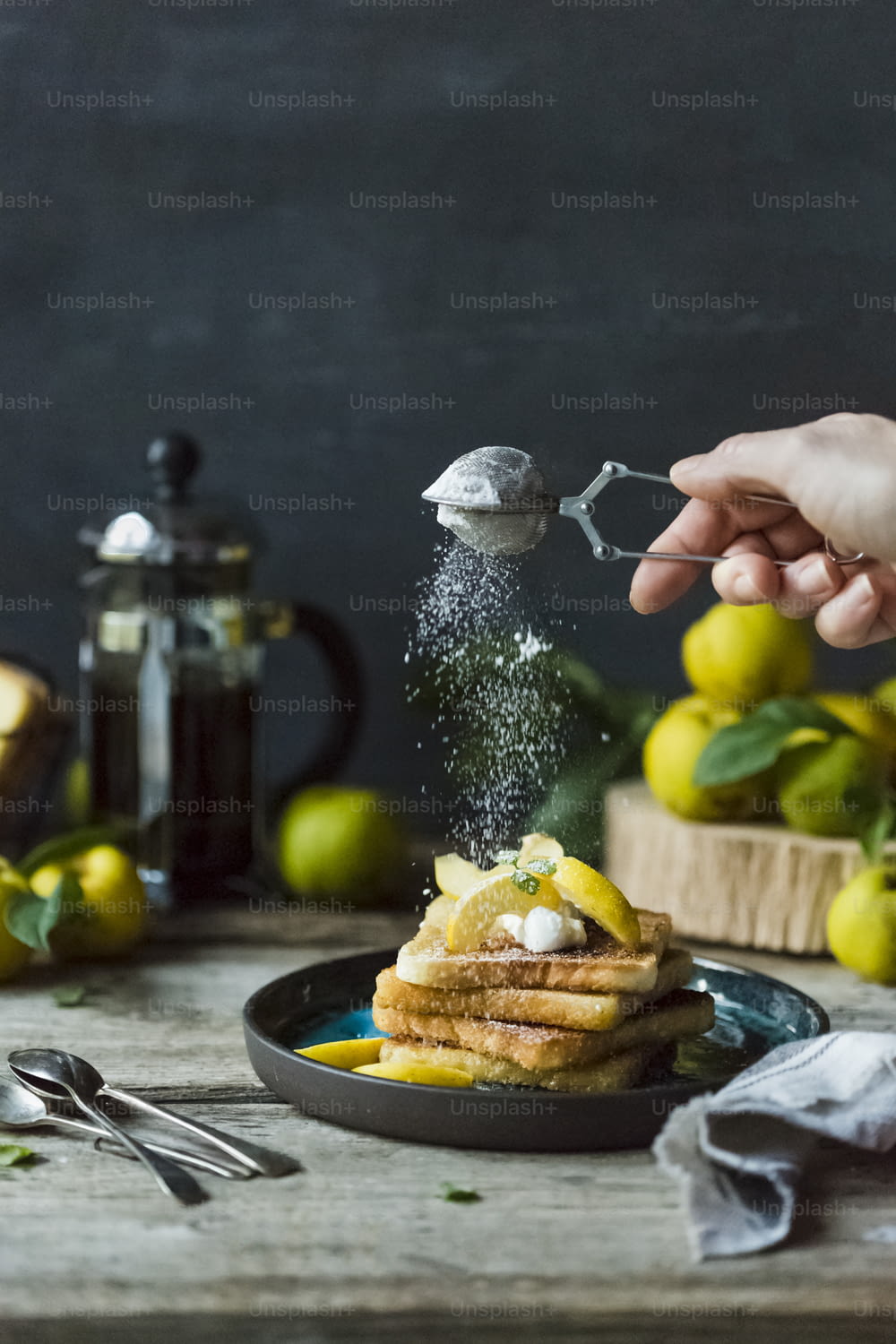 a person sprinkling sugar on a stack of pancakes
