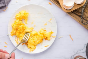 un piatto bianco condito con uova strapazzate e una forchetta