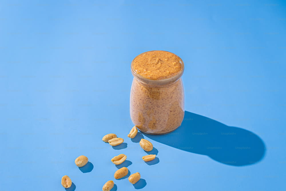 a jar of peanut butter next to peanuts on a blue background
