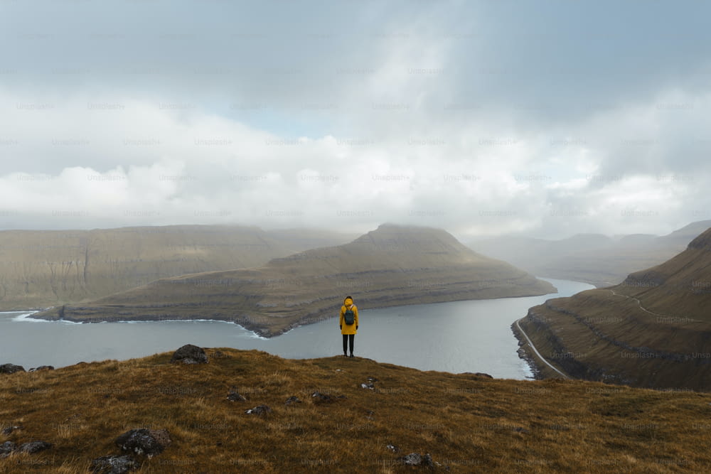 uma pessoa em pé em uma colina com vista para um corpo de água