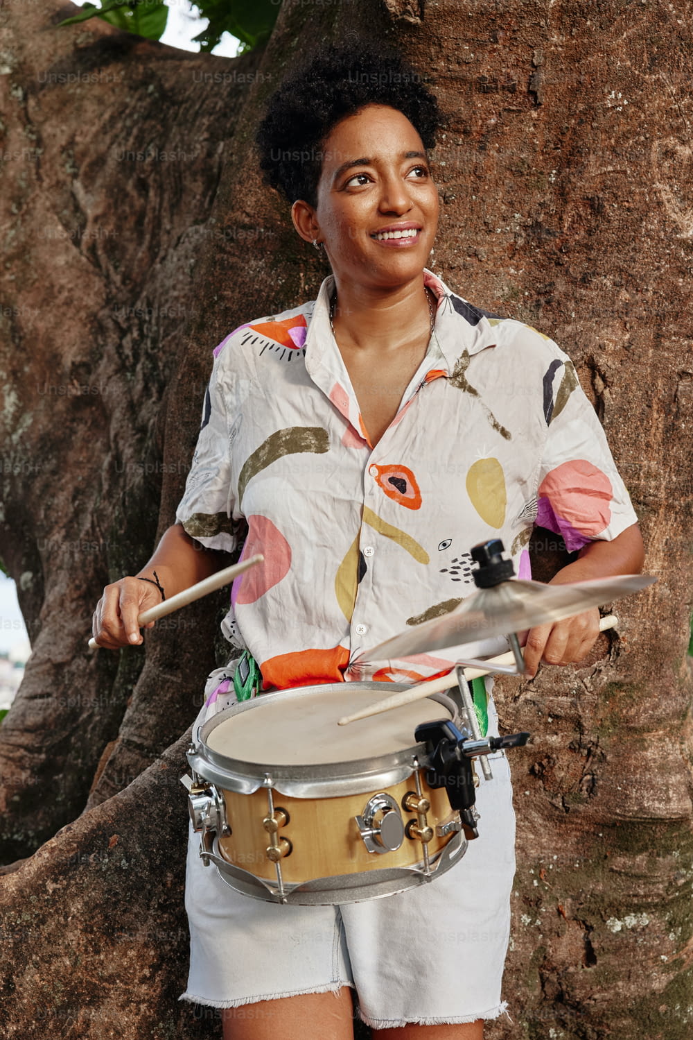 a woman holding a drum in front of a tree