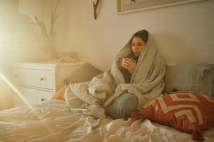 eine Frau, die in eine Decke gewickelt auf einem Bett sitzt