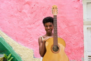 un giovane che tiene in mano una chitarra davanti a un muro rosa