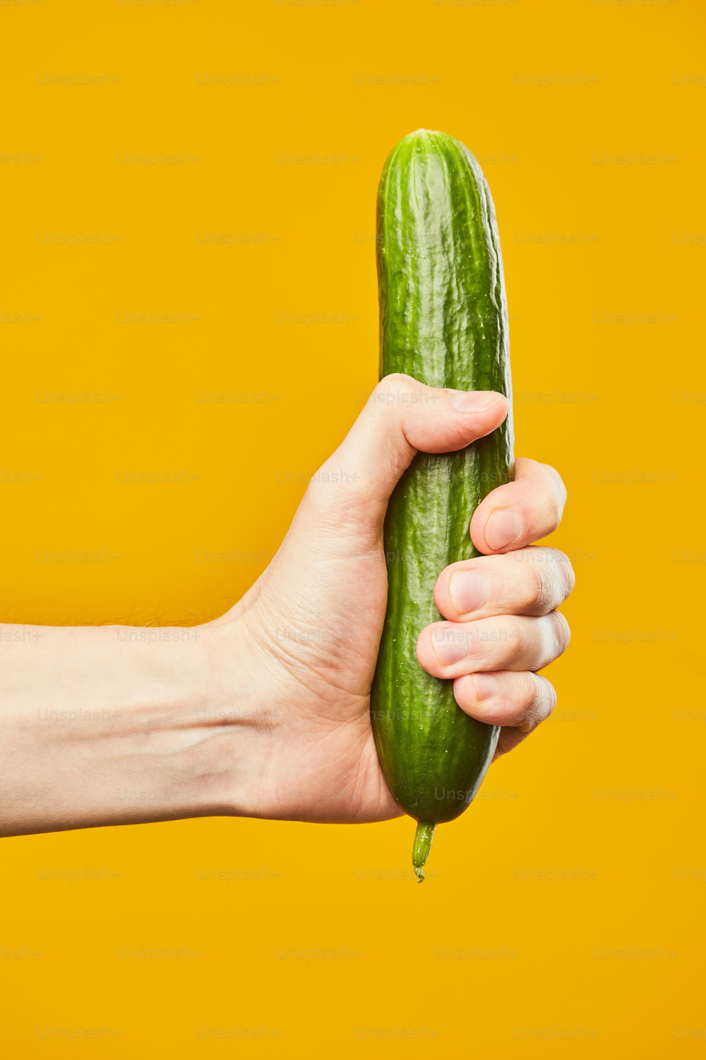 Vibrant shot of hand holding cucumber on yellow background safe sex concept