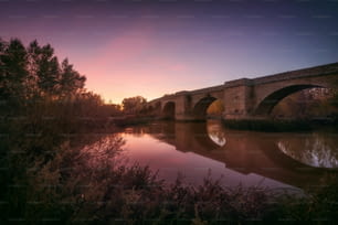 素晴らしい風景。美しい色とりどりの夕暮れ時の静かな川に架かる中世の橋。
