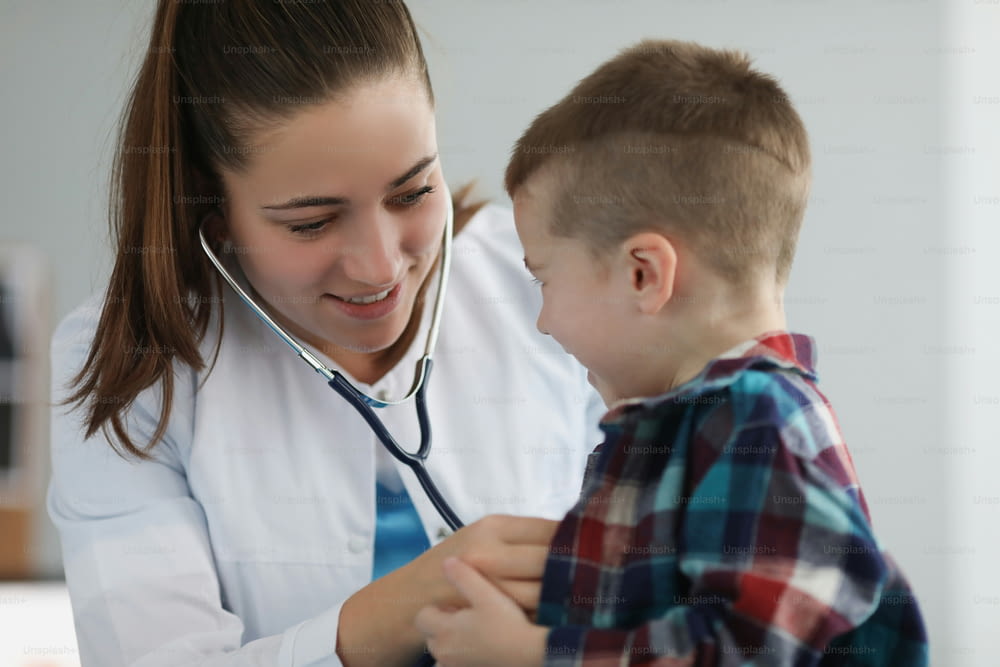 Portrait of young woman pediatrician listen kid with stethoscope tool on planned checkup. Appointment in clinic to examine health condition. Health concept