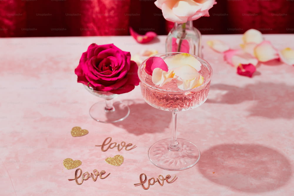 a pink table with two wine glasses and a rose