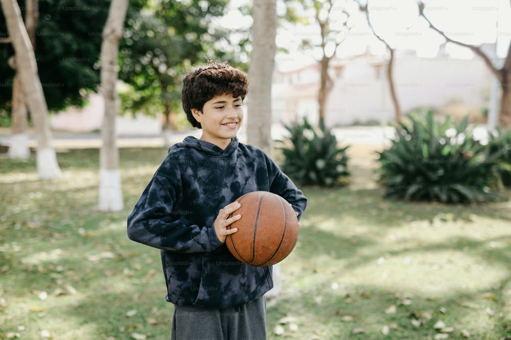 a young boy holding a basketball in a park