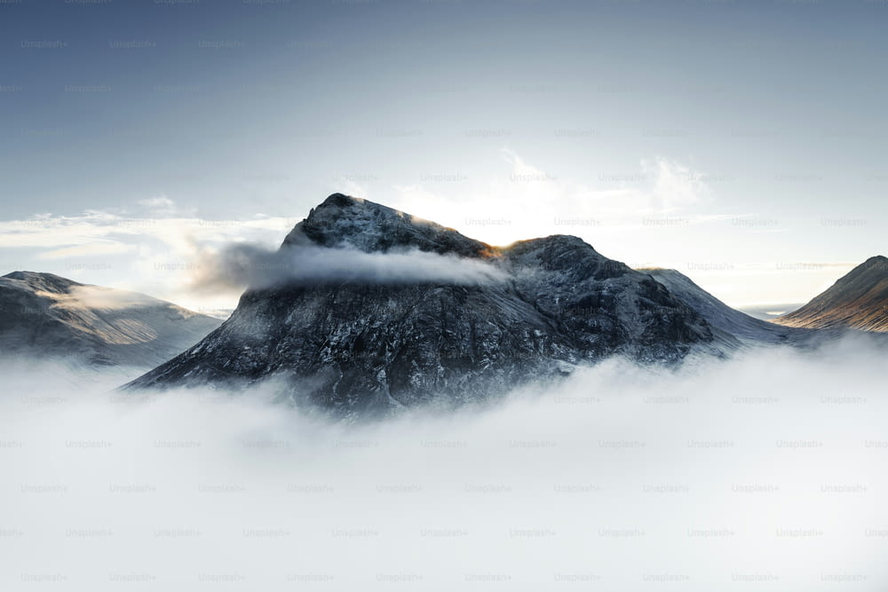 uma montanha coberta de nevoeiro e nuvens sob um céu azul