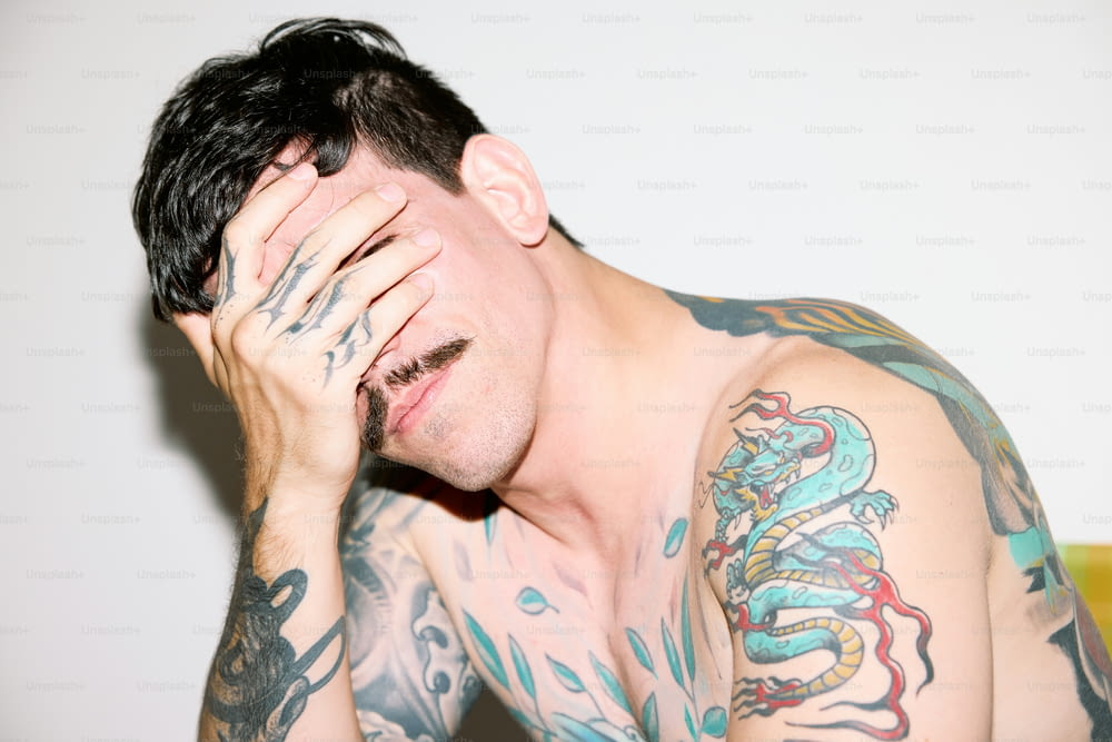 a man with tattoos covers his face with his hands