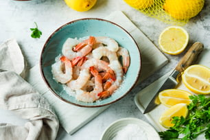 a bowl filled with shrimp next to lemons and parsley