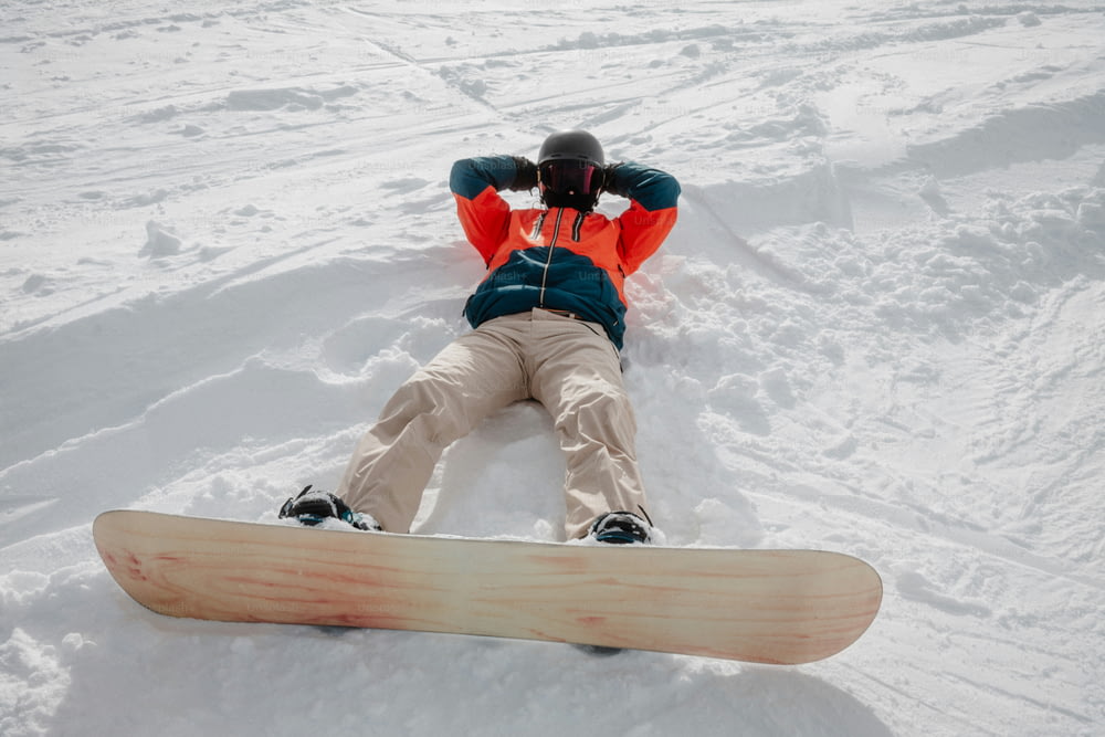 uma pessoa deitada na neve com uma prancha de snowboard