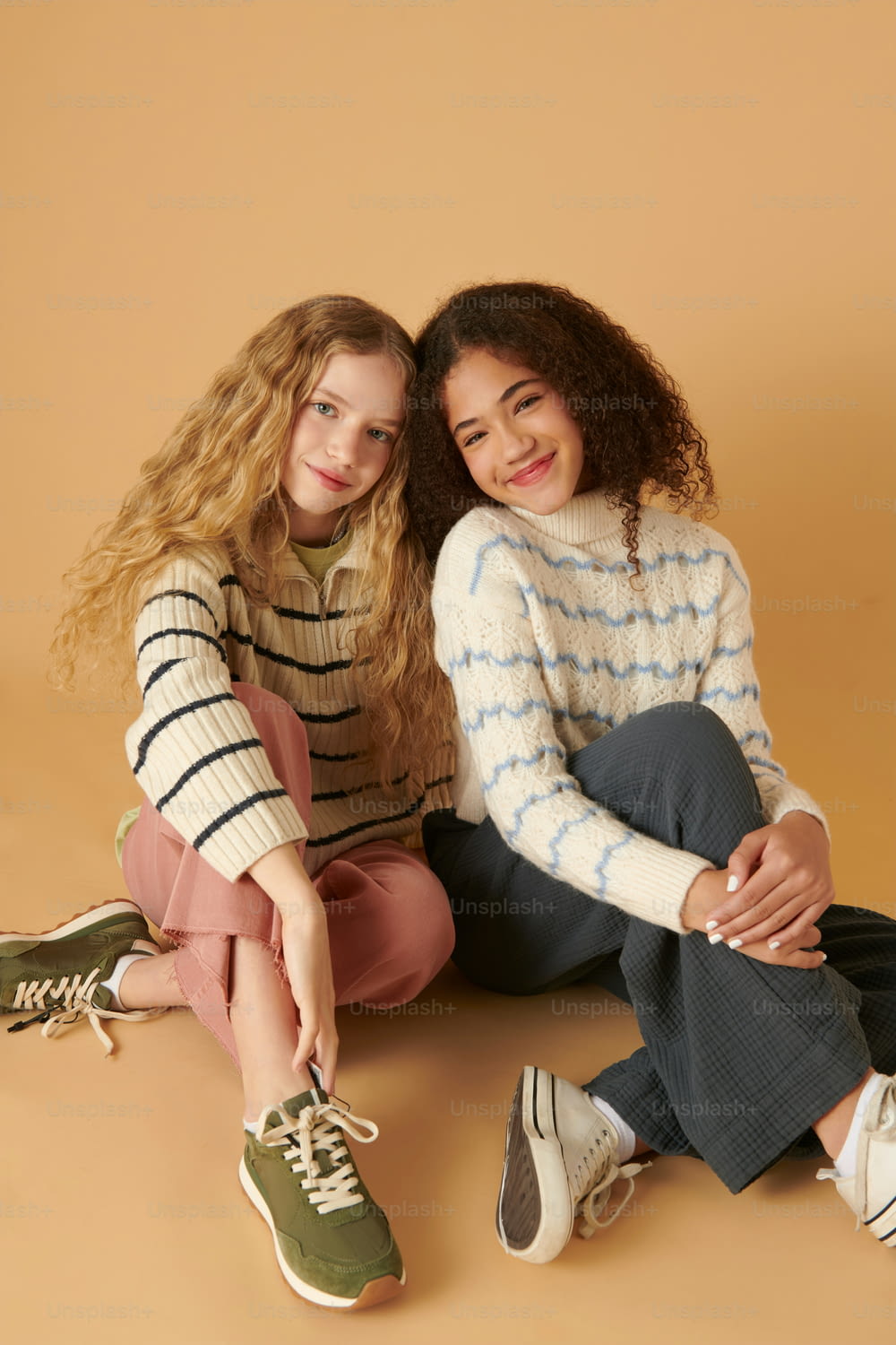 two girls sitting on the ground posing for a picture