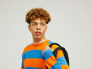 um jovem de cabelos cacheados vestindo um suéter listrado laranja e azul