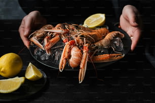 a person holding a plate of cooked lobsters