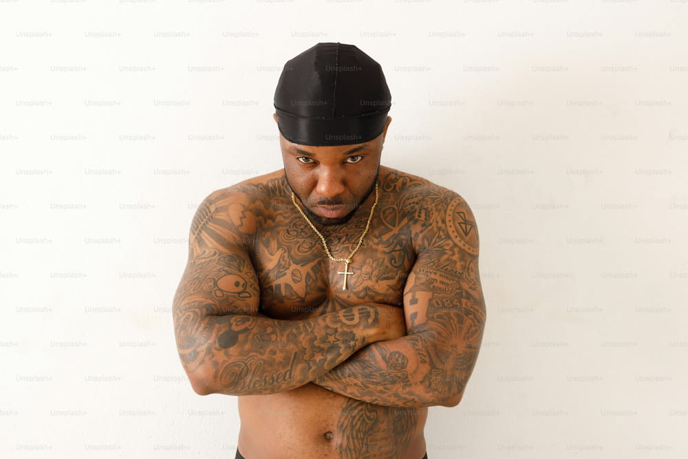 a man with tattoos and a hat standing with his arms crossed