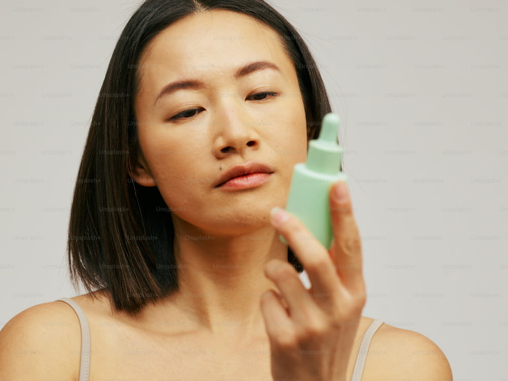 una mujer sosteniendo una botella verde de loción frente a su cara