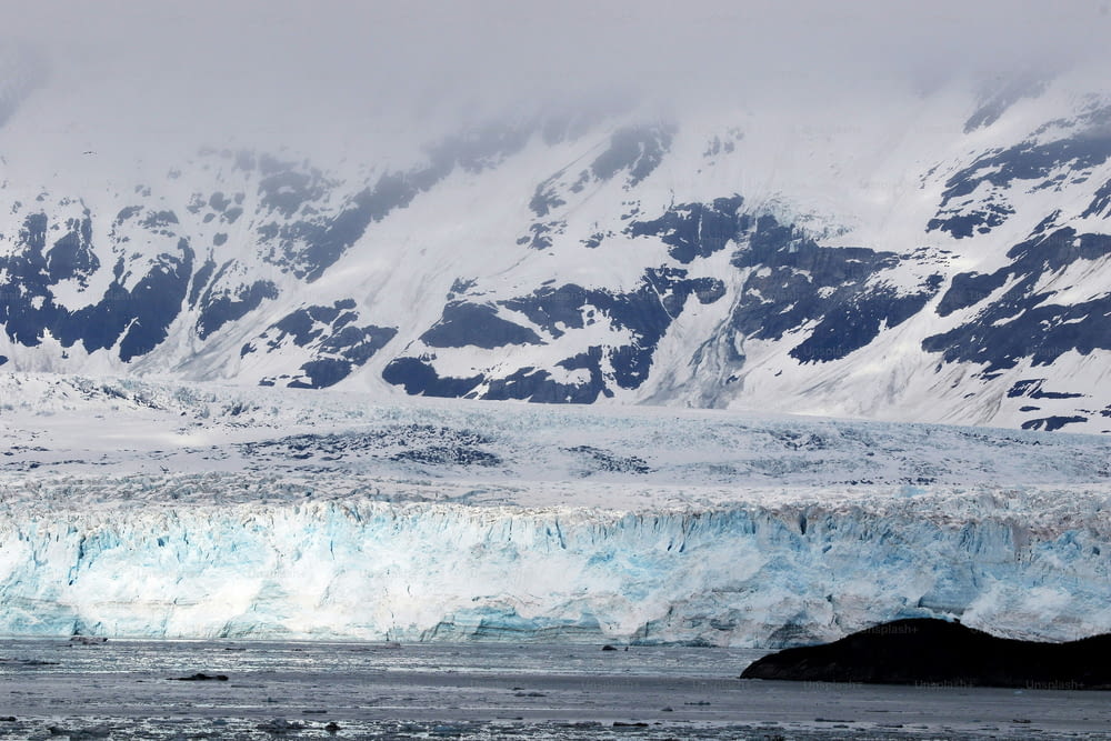 a large glacier with snow covered mountains in the background