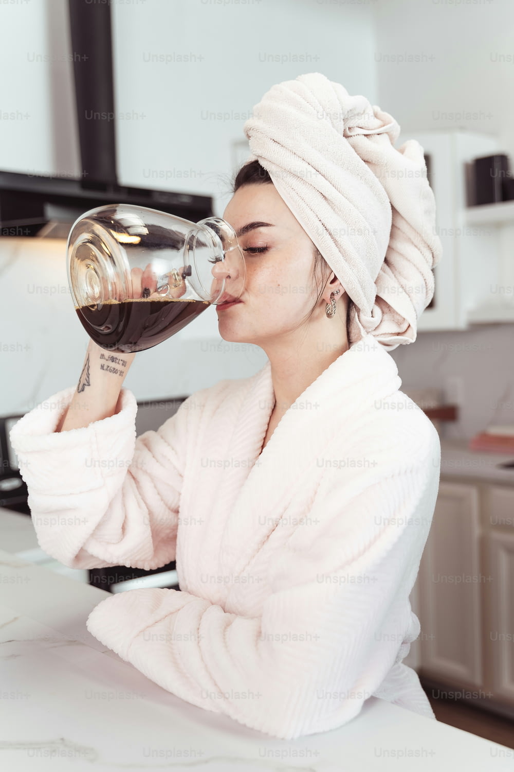 eine Frau mit einem Handtuch auf dem Kopf, die aus einem Weinglas trinkt