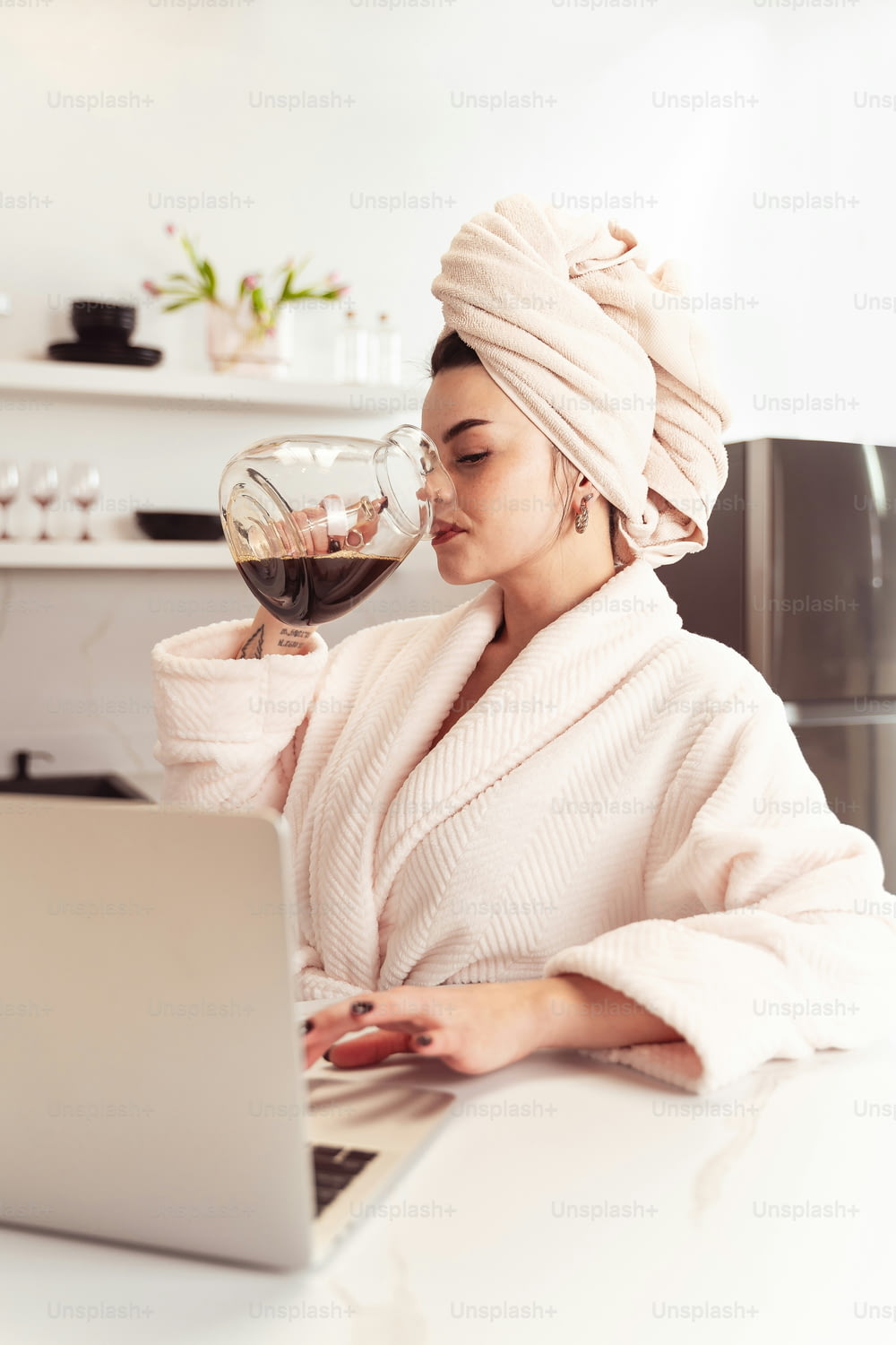 a woman in a bathrobe drinking a glass of wine while using a laptop