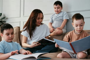 a woman sitting on a couch reading a book to two boys