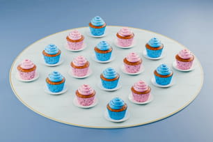 ein weißer Teller mit blauen und rosa Cupcakes