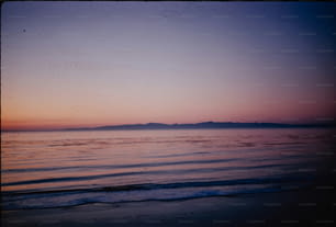 a view of a beach at sunset with a mountain in the distance