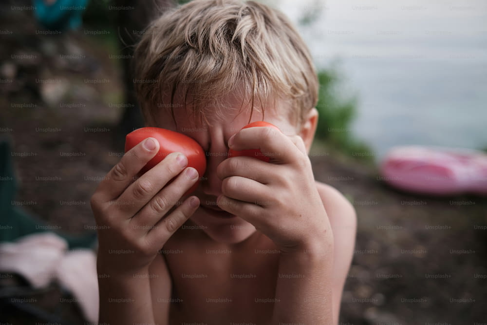 a young boy holding a tomato in front of his face