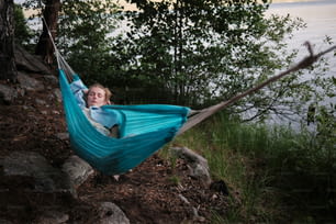 a little boy laying in a hammock by the water