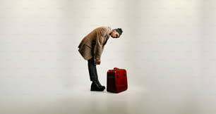 赤いスーツケースの隣に立つ男