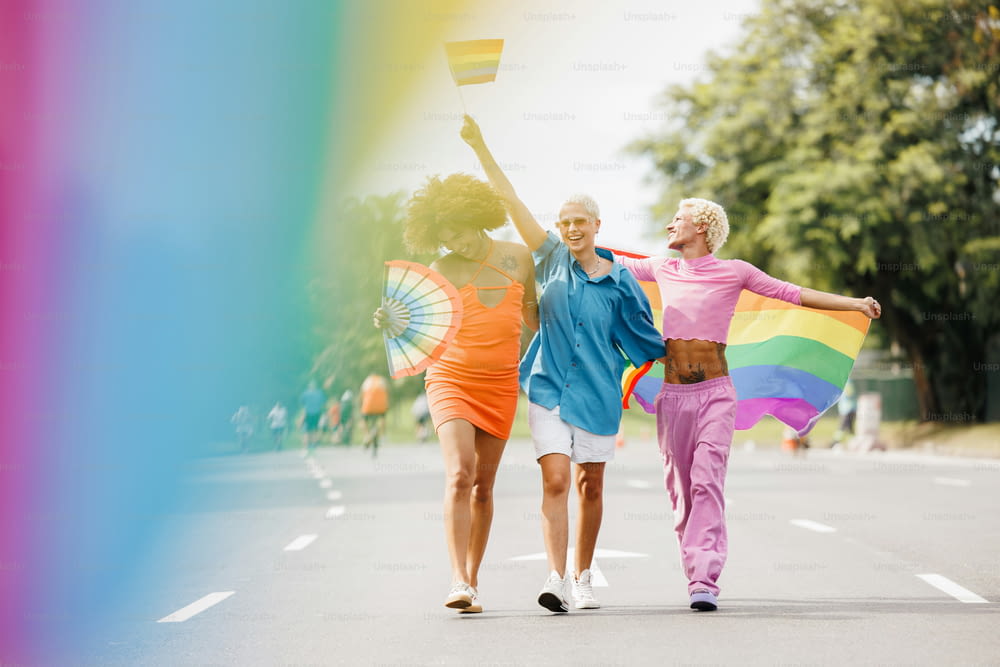 three women walking down a street holding a rainbow flag