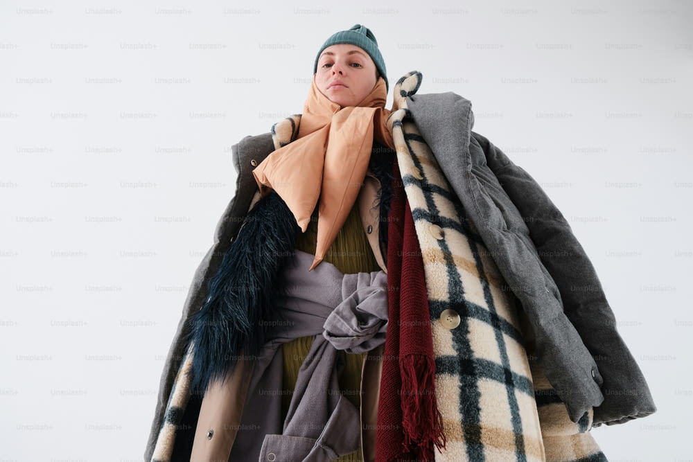 a woman is holding a pile of coats