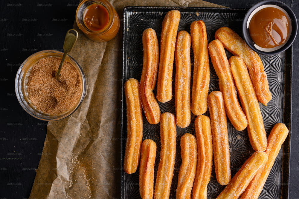 a tray of churros next to a cup of sauce