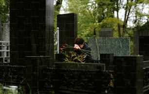 una donna seduta in un cimitero con le mani sul viso