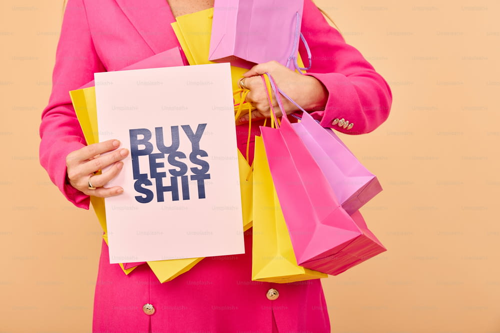 a woman holding a sign that says buy less shit