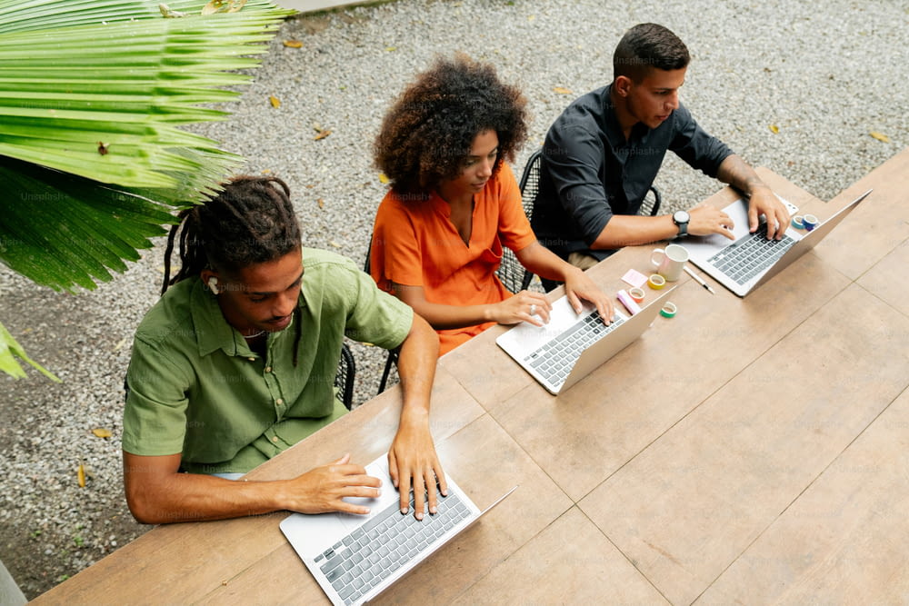 three people sitting at a table with laptops