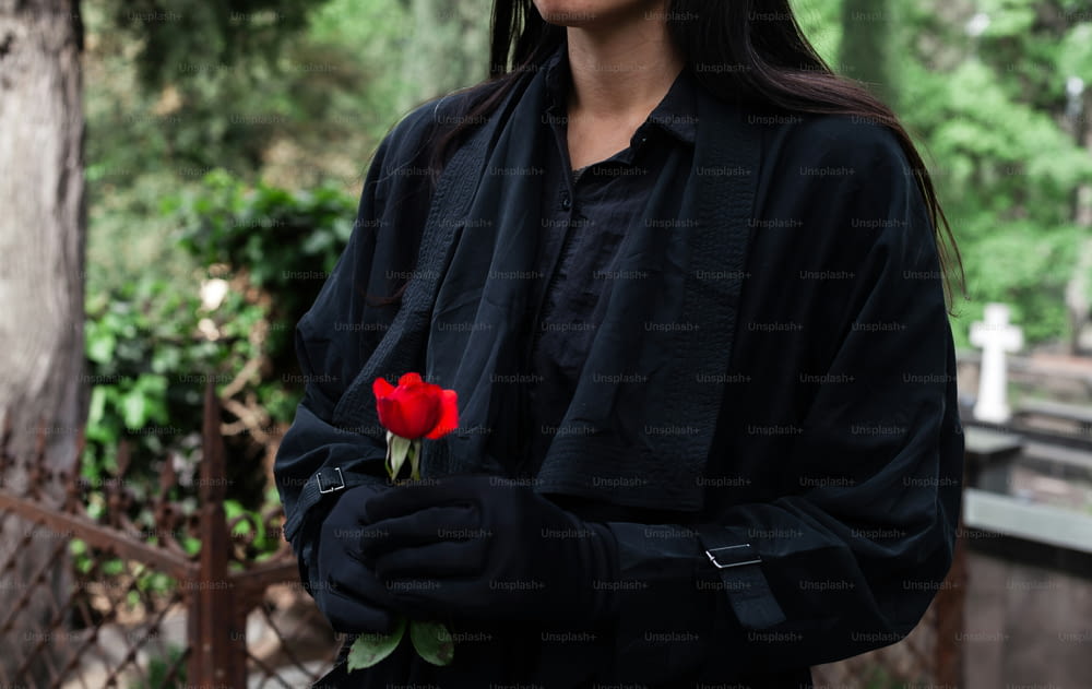 une femme en veste noire tenant une rose rouge
