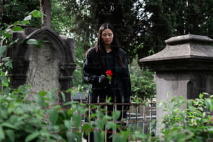 eine Frau, die mit einer Rose in der Hand auf einem Friedhof steht