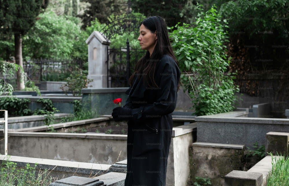 une femme debout dans un cimetière avec une rose à la main