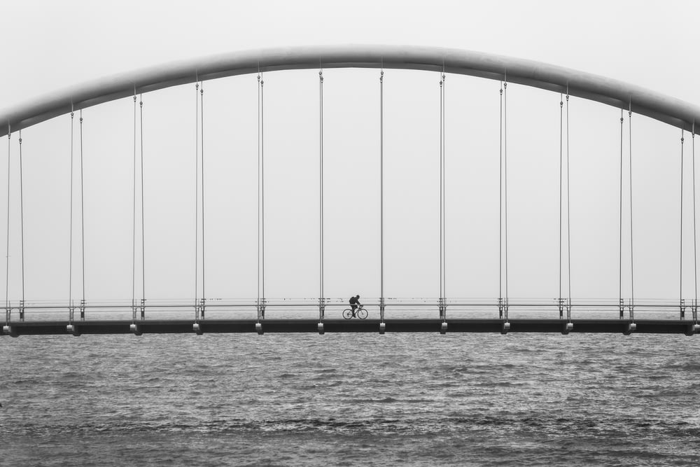 gray scale photo of person driving bike on bridge
